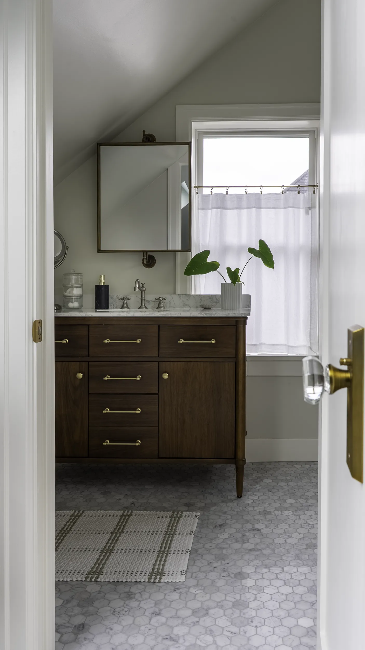 Walnut vanity with marble counter, brushed brass hardware, and a standoff mirror floating over the window