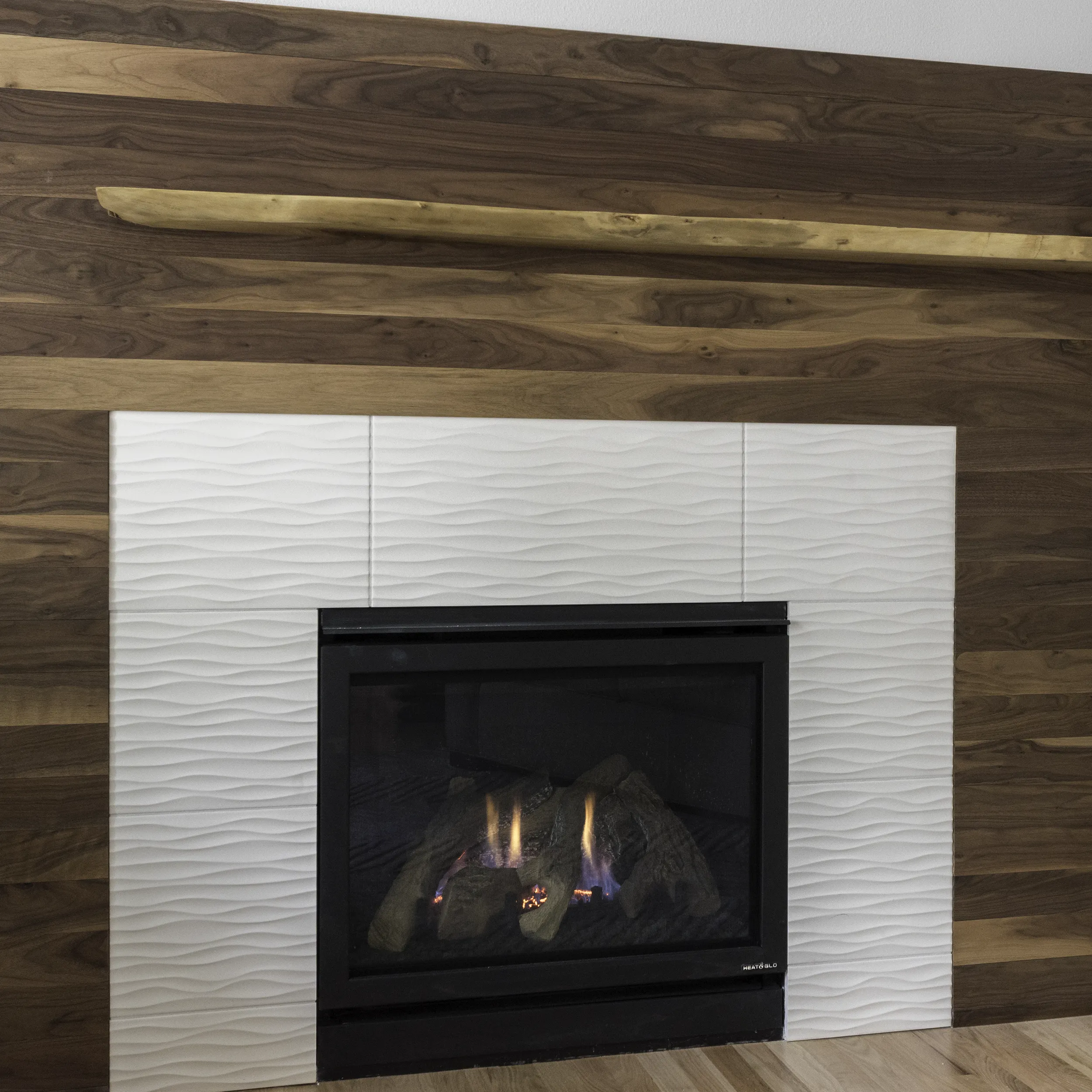 Detail of live-edge walnut mantel and white wave-textured tile around the den firebox