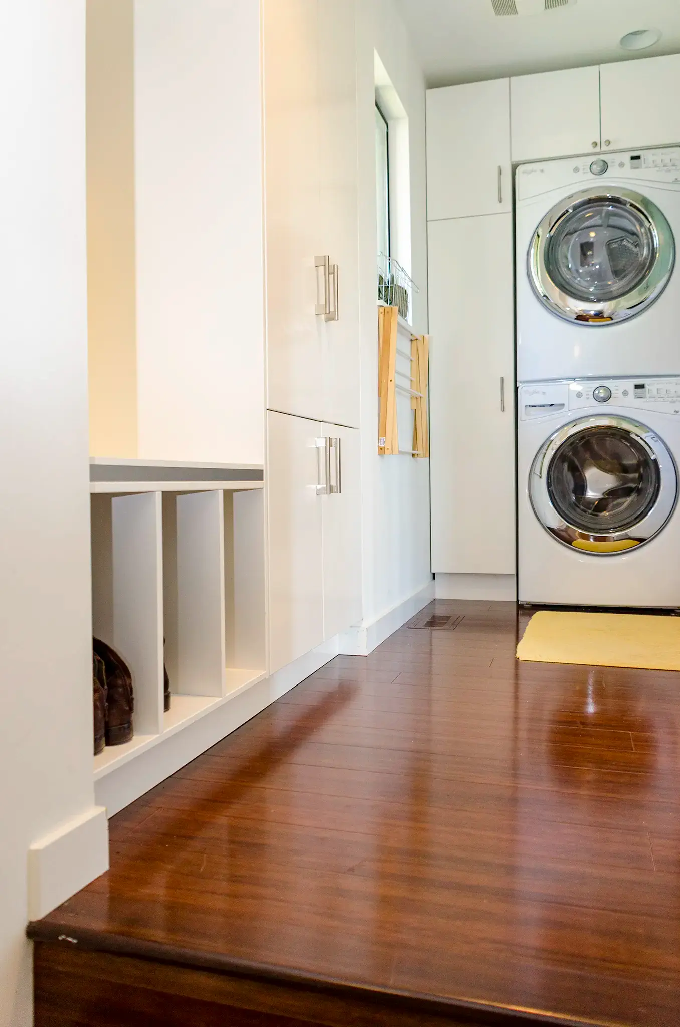 Laundry room and mudroom combo with white cabinets, boot cubbies and a stacked washer and dryer